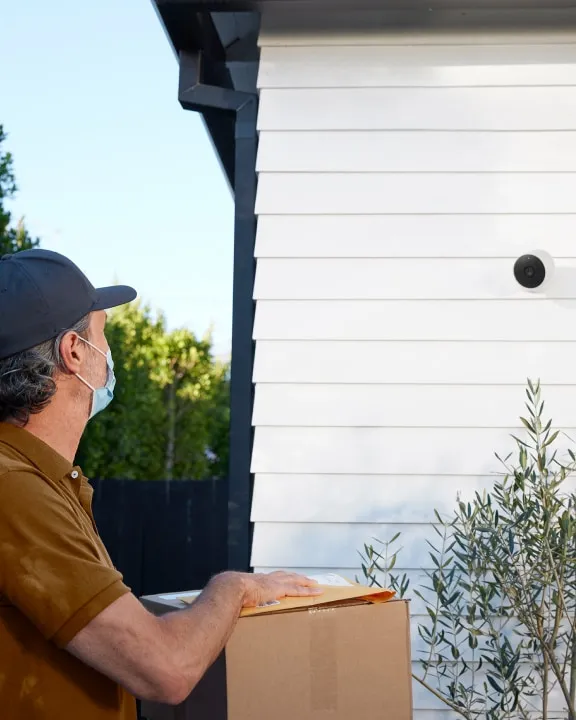Google Nest Cam (battery) mounted on white house siding as a delivery driver arrives
