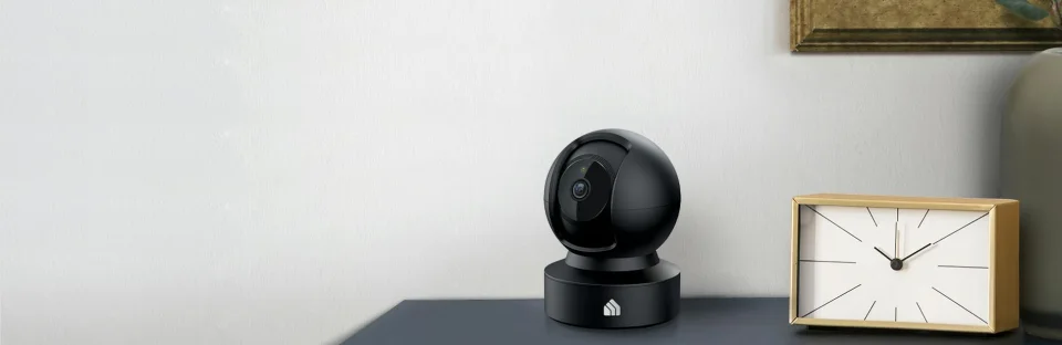 Black Kasa EC71 pan-tilt camera sitting on a table next to a clock