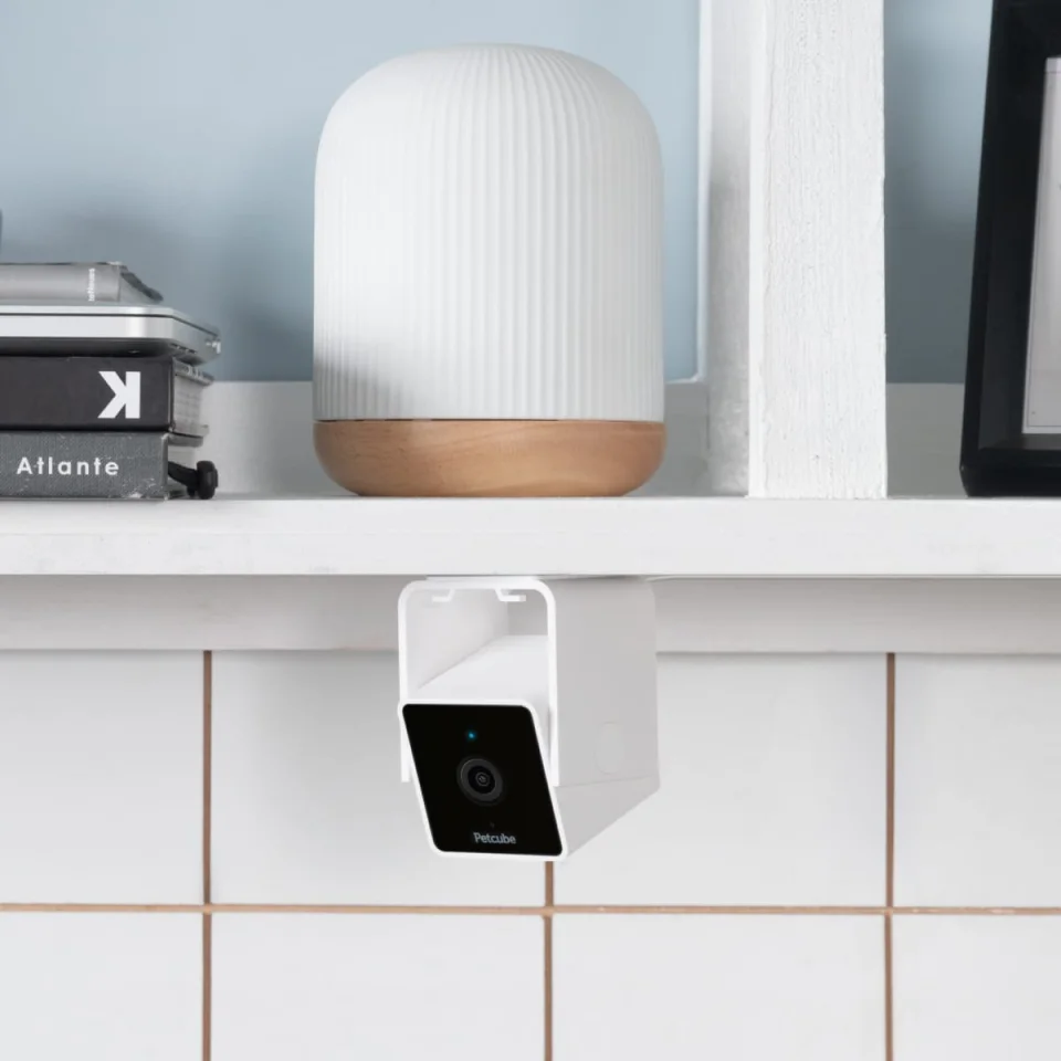 Petcube Cam mounted upside down under a shelf above white tiles