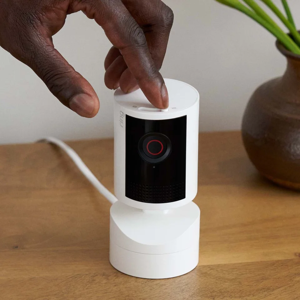 Hand sliding the built-in privacy shutter switch on top of a white Ring Pan-Tilt Indoor Cam 2K