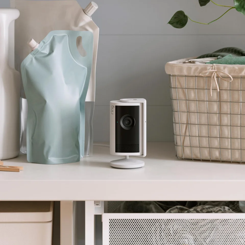 Ring Indoor Cam Plus in white on a laundry-room shelf between household items