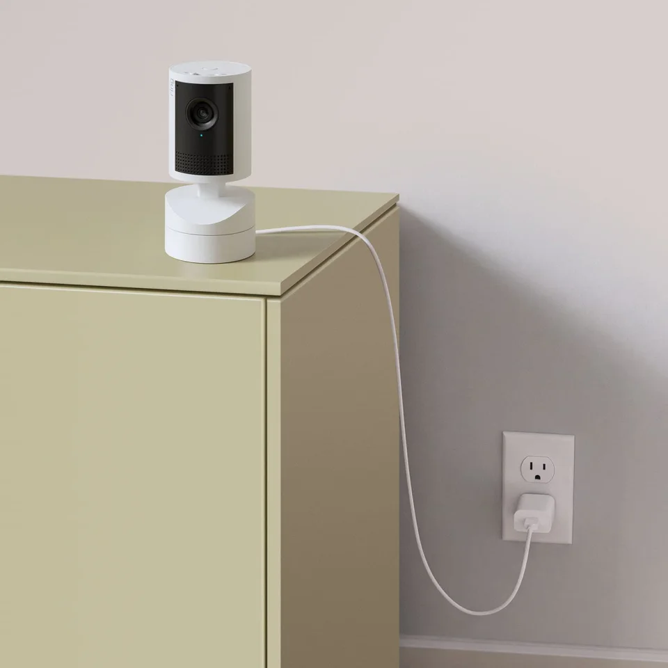 Ring Pan-Tilt Indoor Cam 2K in white on top of a cabinet, plugged into a wall outlet