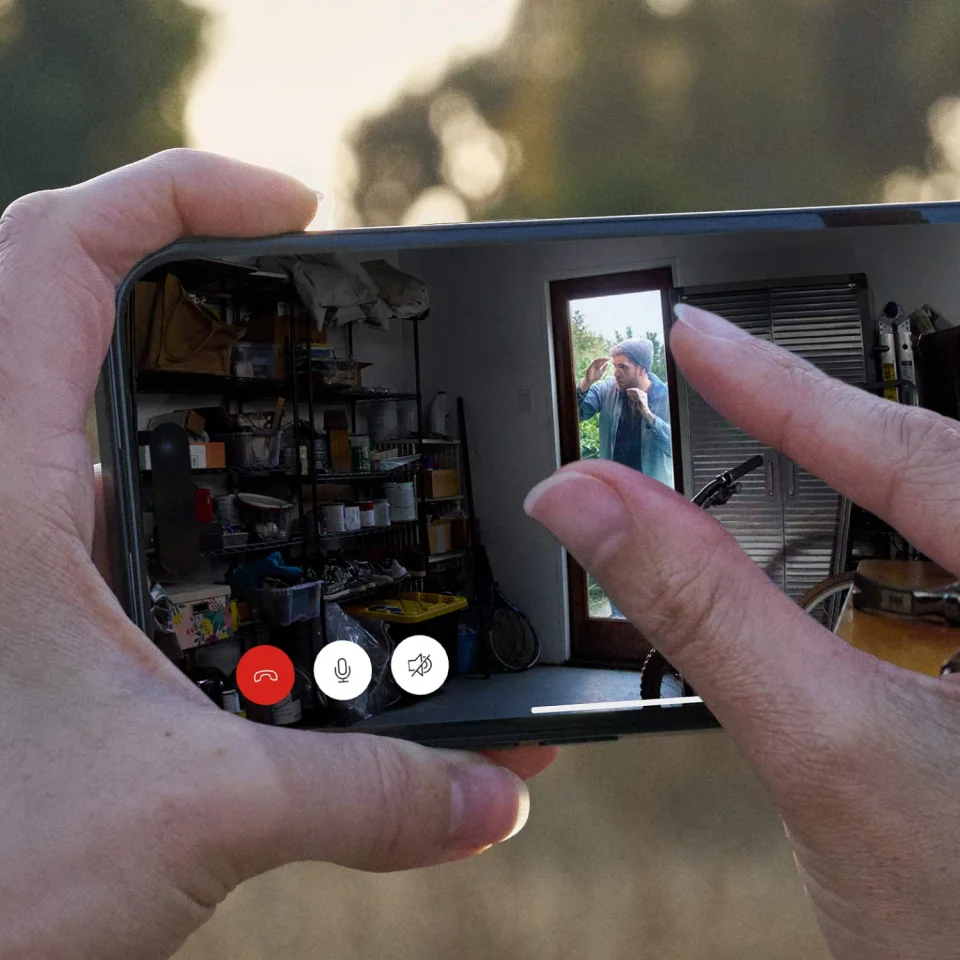 Hands holding a phone showing a Ring Indoor Cam Plus live view with pinch-to-zoom