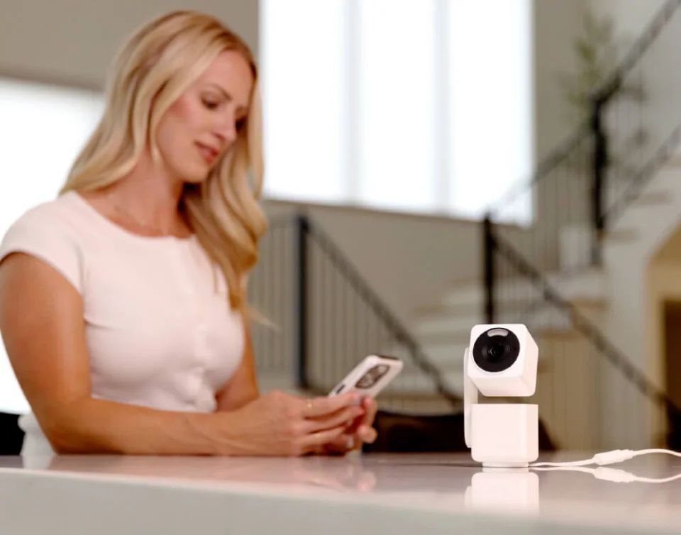 Wyze Cam Pan v4 in white on a kitchen counter while its owner uses the Wyze app on a phone