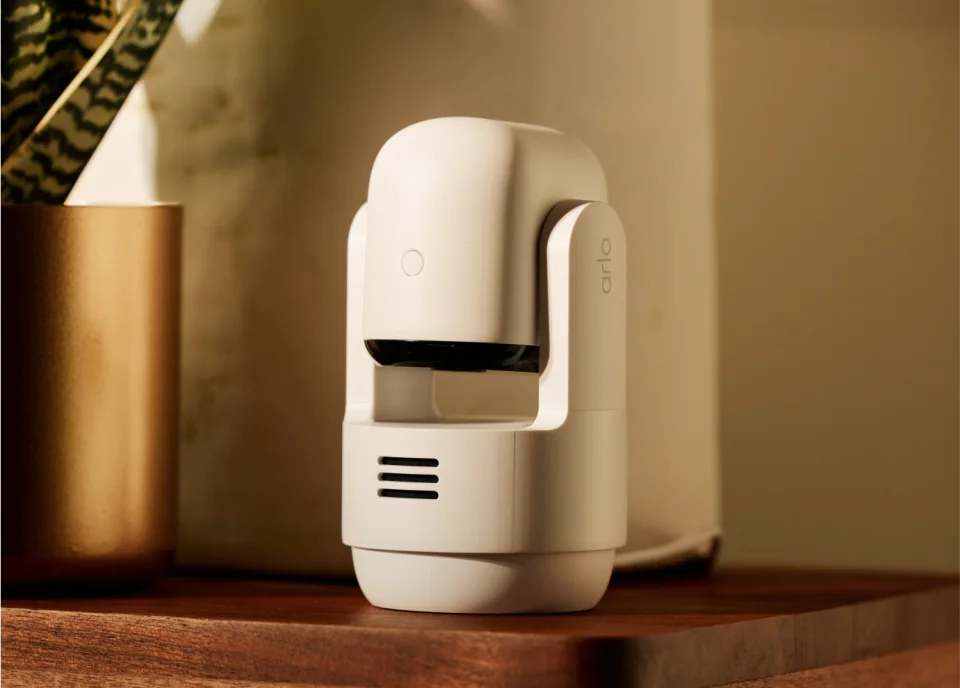 Arlo Essential Pan Tilt Indoor camera on a wooden surface with its lens tilted down and Arlo branding on the arm