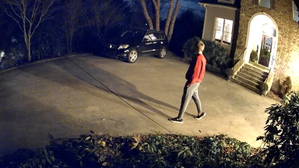 Official Wyze Color Night Vision sample frame from the Cam Pan v3 showing a person in a red top walking toward a house entrance at night