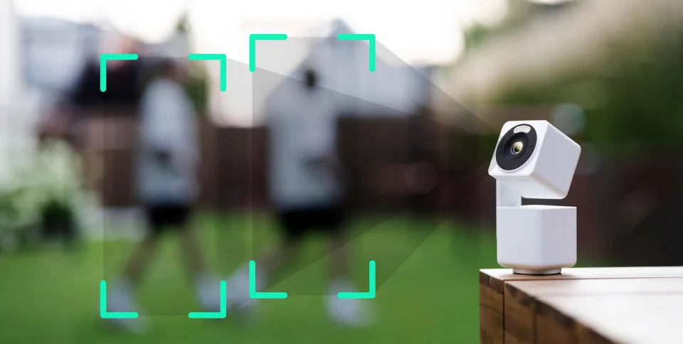 Wyze Cam Pan v4 outdoors on a wooden surface with AI tracking brackets following people in a garden